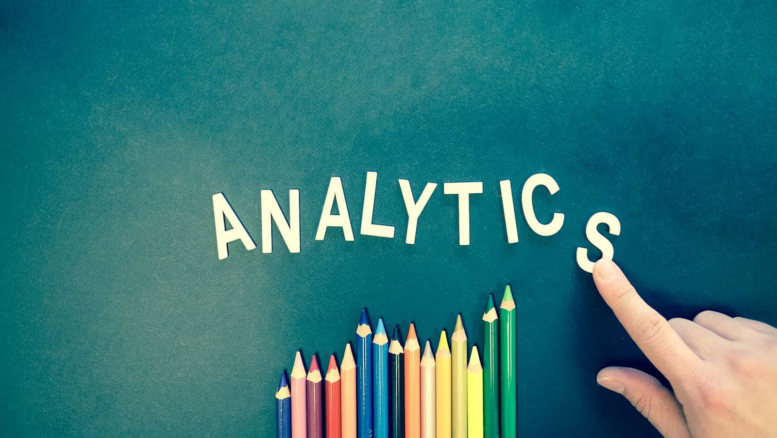 Uma mão a organizar peças de letras que formam a palavra "Google Analytics" acima de um fila de lápis coloridos Uma mão a organizar peças de letras que formam a palavra "Google Analytics" acima de um fila de lápis coloridos